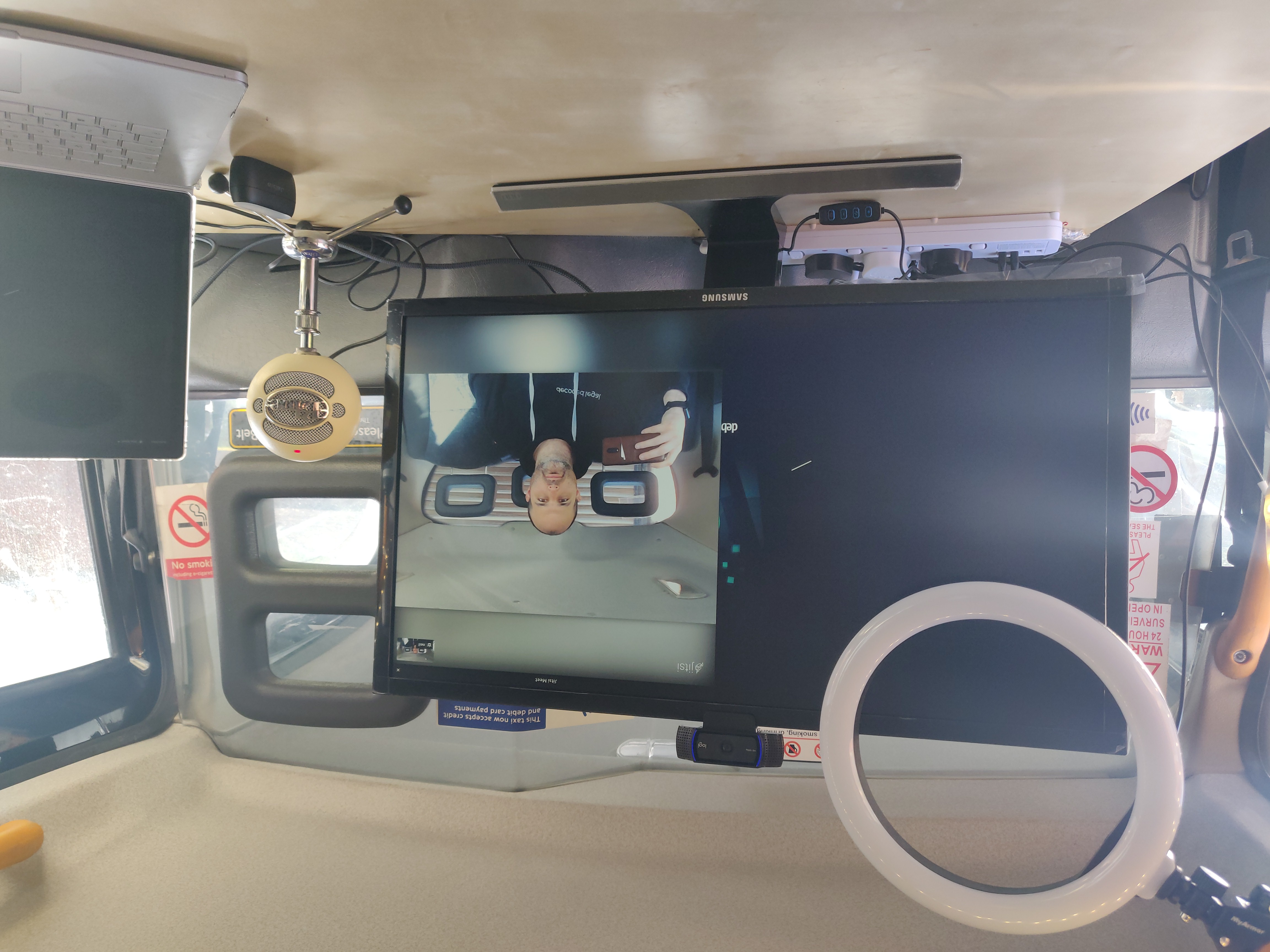 Photo of a screen and laptop on a light wood desk, in the back of a taxi