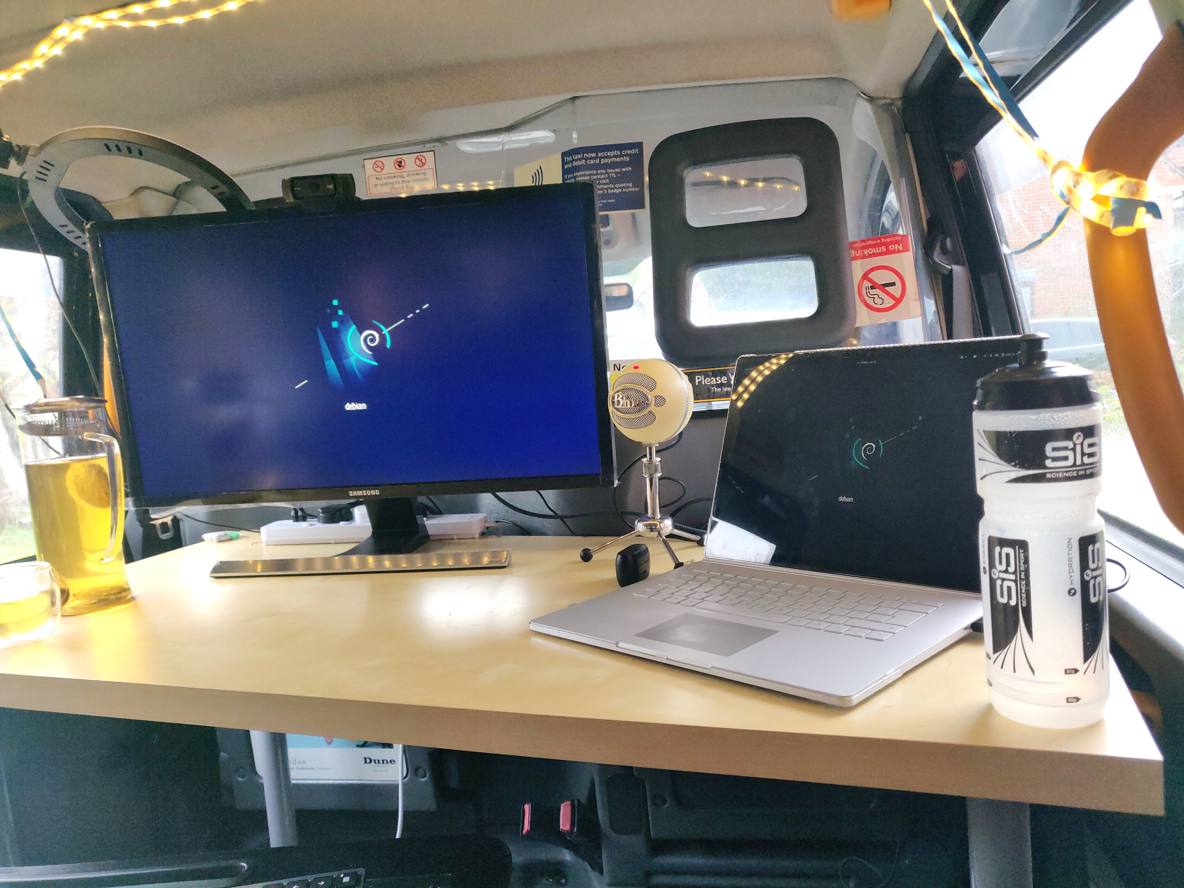 Photo from the rear right hand seat of the taxi, looking at my desk, with a screen and laptop on it, and a bottle of water and a jug of green tea