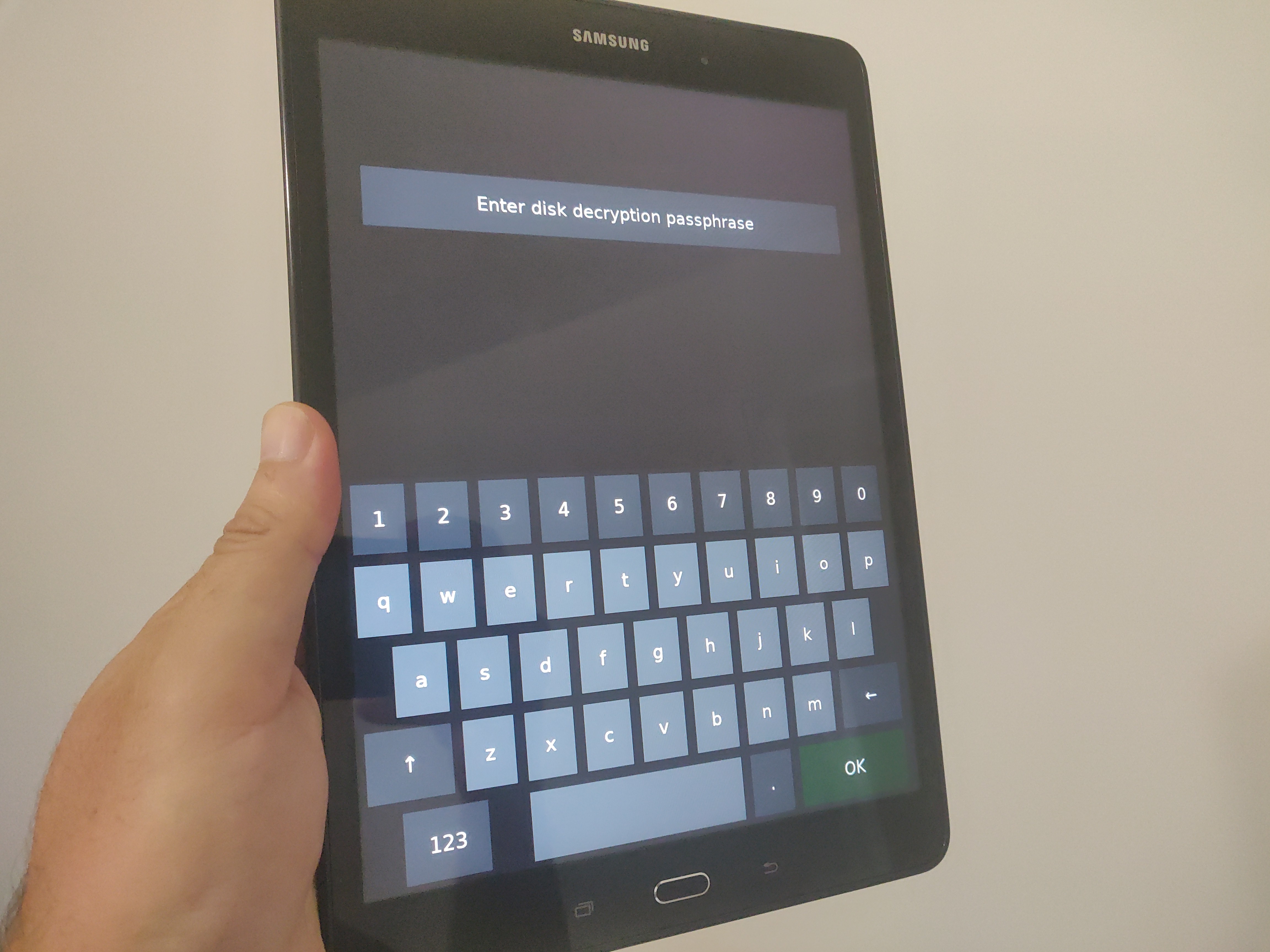 Photo of a black Samsung Galaxy Tab, being held on the lefthand side in portrait orientation, showing the full disk encryption unlocking screen