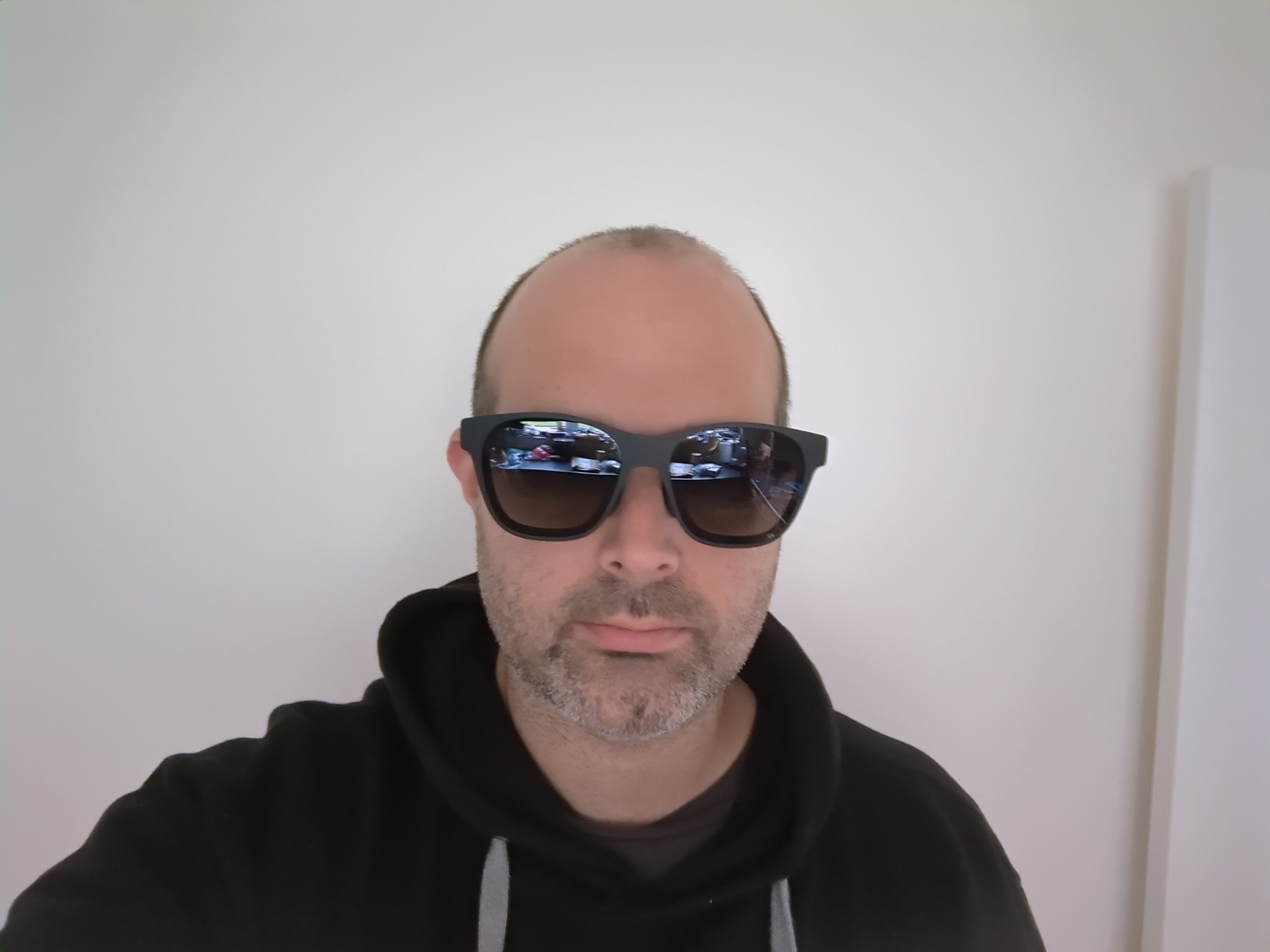 Photo of me - white man, not much hair, black hoodie - wearing a pair of Xreal glasses. They look like large black sunglasses.