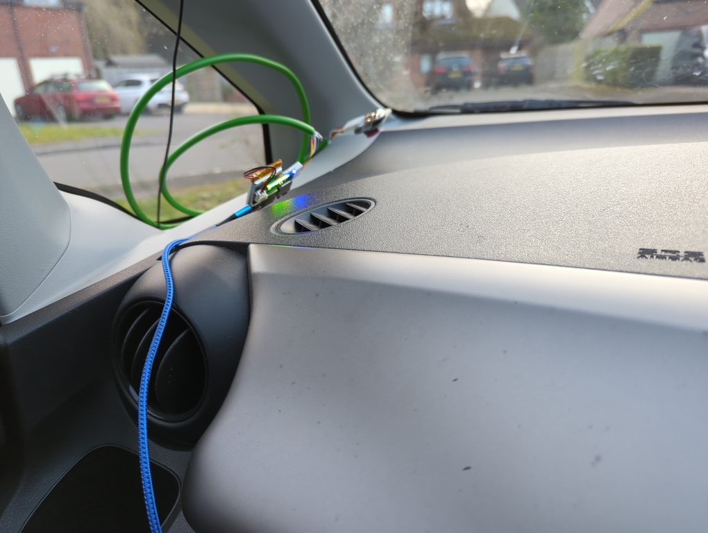Photo of a small circuit board on the dash of a car. It is connected to a blue USB-C cable. Connected to the circuit board, by a thick-ish green cable, is an even smaller circuit board, the GPS receiver.